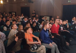 Publiczność w teatrze patrząca w stronę sceny i obserwująca sztukę.
