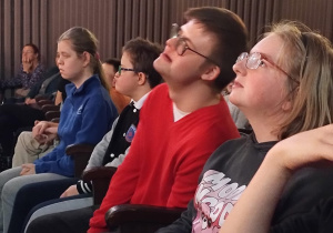 Na zdjęciu widoczni są uczniowie, siedzący wśród publiczności i obserwujący wydarzenia na scenie.