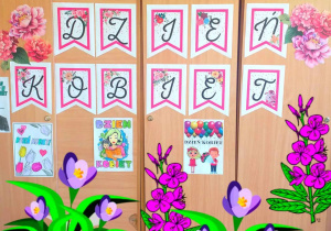 Dekoracja świetlicowa. Wielki napis "DZIEŃ KOBIET", wokół ponaklejane są kolorowe kwiaty