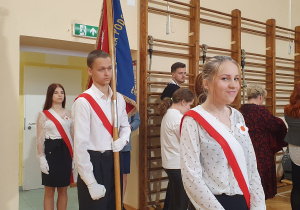 Uczniowie stoją w szeregu - honorowa asysta niosąca flagę Polski.