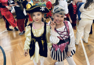 Dwie dziewczynki w kostiumach piratek uśmiechają się do zdjęcia podczas szkolnego balu karnawałowego.
