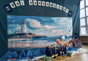 Scenografia balu karnawałowego w stylu pirackim: latarnia morska, statek, skrzynia ze skarbem i dekoracje morskie.