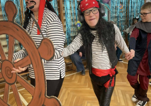 Dzieci przebrane za piratów biorą udział w zabawie, jedno trzyma ster statku podczas szkolnego balu.