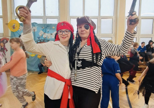 Dwie osoby w strojach piratów stoją razem i unoszą zabawkowe szable podczas balu karnawałowego.