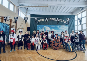 Grupowe zdjęcie dzieci i dorosłych w kostiumach pirackich na tle dekoracji balu karnawałowego w sali gimnastycznej.