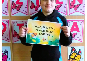 Zdjęcie przedstawia ucznia trzymającego kartkę z napisem.