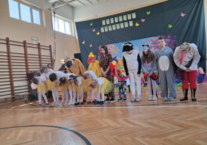 Dzieci w kostiumach zwierząt i tancerki kłaniają się publiczności po występie na szkolnej scenie.