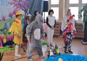 Dzieci w kostiumach (m.in. królik, ptak, owca) stoją wokół dekoracji stawu.